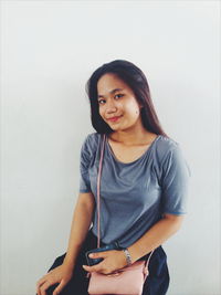 Portrait of smiling young woman sitting against wall