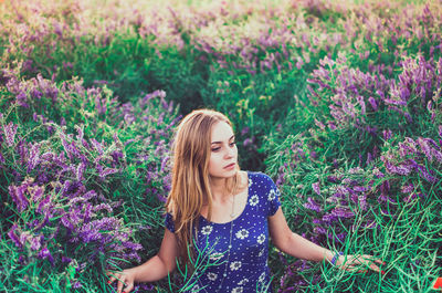 Slim girl walks on tall grass overgrown with purple flowers. women's blue dress white daisy print