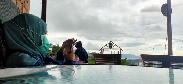 Rear view of people sitting on shore against sky