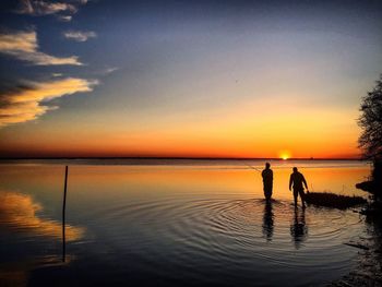 Silhouette people standing in lake against sky during sunset