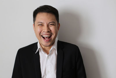 Close-up portrait of cheerful man wearing blazer by white wall