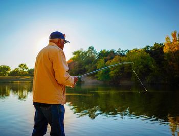 Man fishing in lake against sky