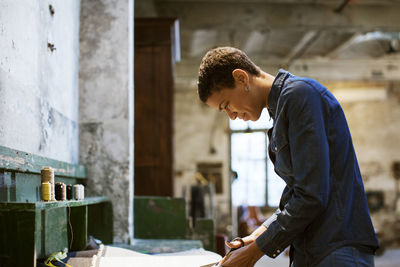 Side view of smiling designer cutting fabric in workshop