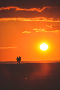 Silhouette people on sea against orange sky during sunset