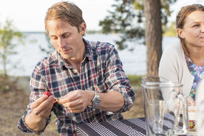 Man cleaning strawberry while having lunch with friends at lakeshore