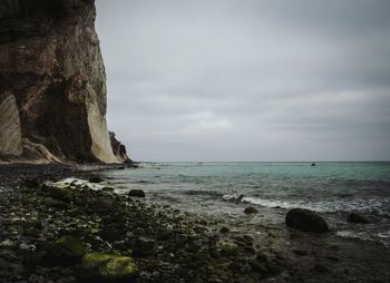 Scenic view of cliff by sea against cloudy sky