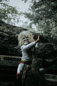 Woman with arms raised standing against trees