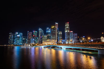 Illuminated buildings by river against sky at night