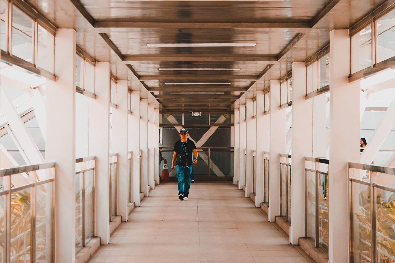 REAR VIEW OF MAN WALKING ON CORRIDOR OF BUILDING