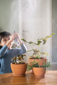 A boy sprays flowers in orange clay terracotta pots with a spray gun.