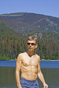 Shirtless mature man wearing sunglasses while standing against lake and mountain at e c manning provincial park