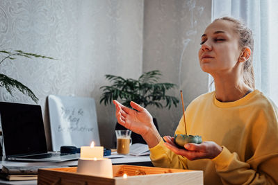 Self care, mental health. young woman sitting near table with lights candles, aroma sticks, enjoy