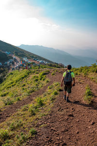 Rear view of man walking on mountain against sky