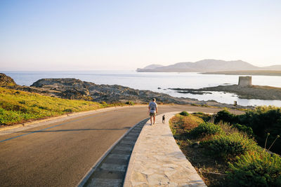 Man with dog walking on sidewalk against sea