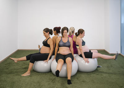 Pregnant woman sitting on fitness ball in round circle with leg up at yoga studio