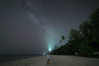 Full length rear view of woman standing with flashlight at beach
