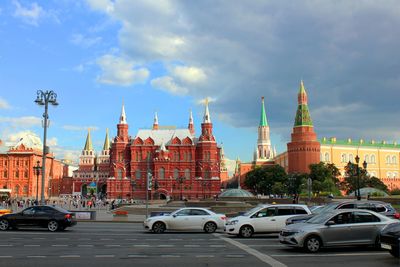 Cars on road by buildings against cloudy sky