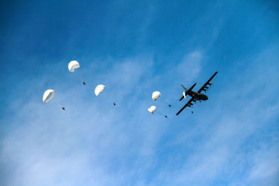 Low angle view of airplane and parachutes flying against blue sky