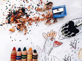 High angle view of colorful crayons with book and pencil shavings on table