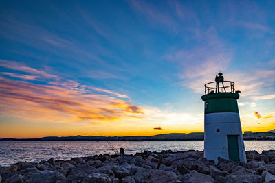 Lighthouse by sea against sky during sunset