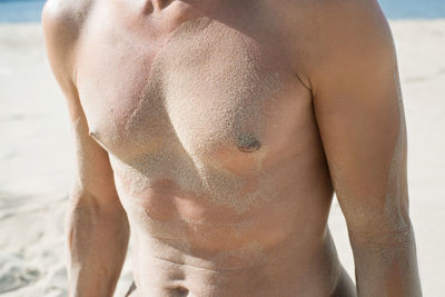 Midsection of man with sand on chest at beach