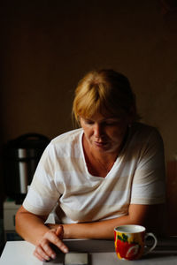 Happy young caucasian woman using mobile phone while sitting at home with coffee or tea mug. morning