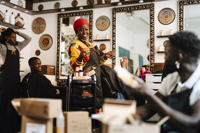 Happy female barber talking with male coworker while working in salon