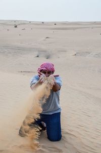 High angle view of mature man playing with sand at desert against clear sky