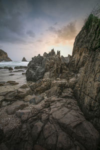 Rock formation on beach against sky during sunset