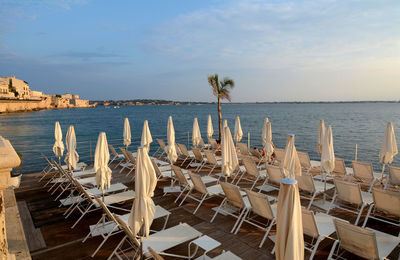 Chairs and tables on beach by sea against sky