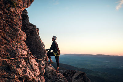 Concept: adventure. climber woman with helmet and harness. silhouette at sunset on the mountain. profile. resting looking at the climbing route. via ferrata in the mountains.