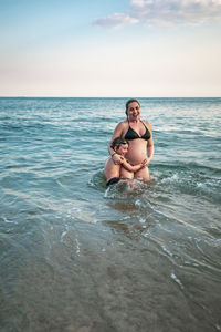 5 years old kid hugging pregnant mother, waist deep in the ocean