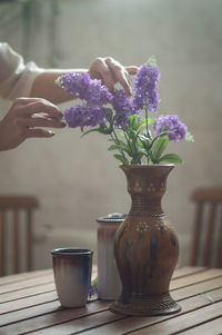 Cropped image of hands holding flowers in vase on table