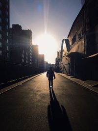 Rear view of young man walking on road amidst buildings on sunny day