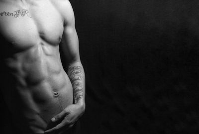 Midsection of shirtless man against black background