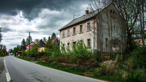 Road amidst trees and buildings against sky