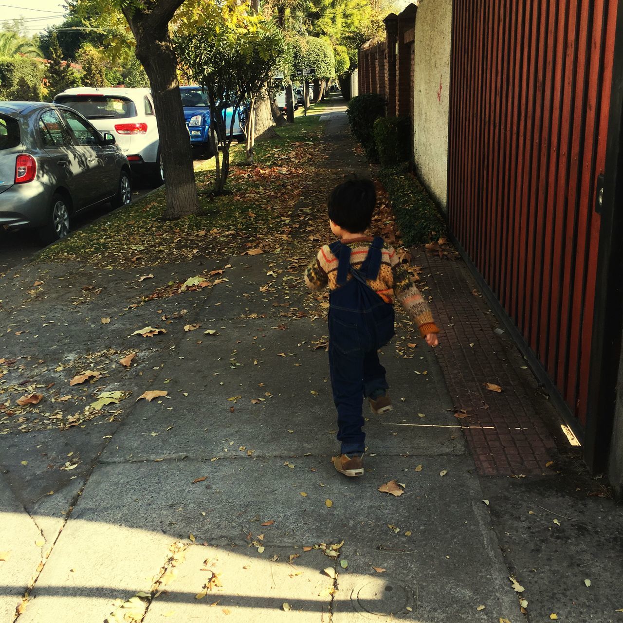 REAR VIEW OF BOY ON SIDEWALK BY STREET