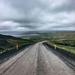 Road passing through field against storm clouds