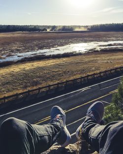 Low section of people standing on road by river against sky