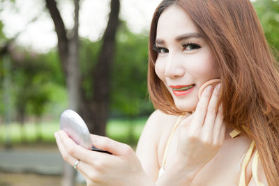 Close-up of young woman with braces applying make-up while sitting outdoors