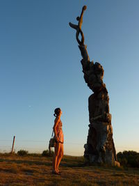 Woman standing by carvings on wood against clear sky