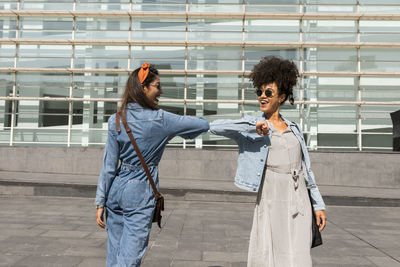 Smiling friends greeting with elbow bumps while standing on rooftop in city