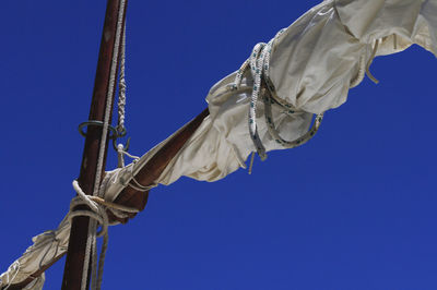 Low angle view of rope and canvas on mast against clear blue sky