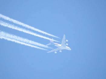 Low angle view of airplane flying against clear blue sky