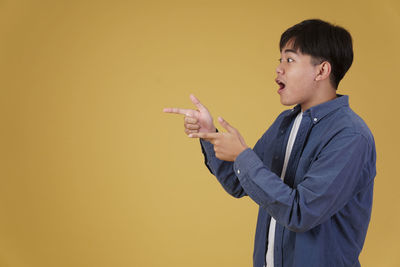 Side view of young man looking away over yellow background