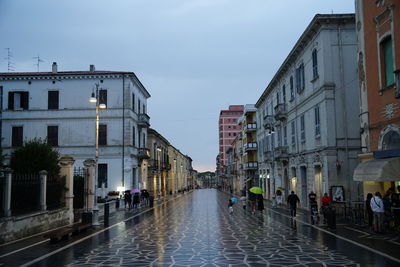 People on wet street amidst buildings in city