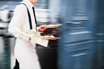 Midsection of chef holding food while walking in restaurant