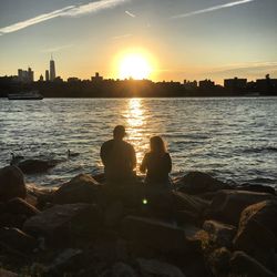 Silhouette of man sitting on shore against sunset sky