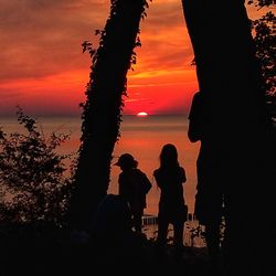 Silhouette people by sea against orange sky during sunset