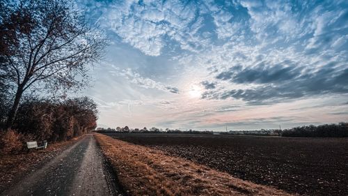Empty road amidst field against sky